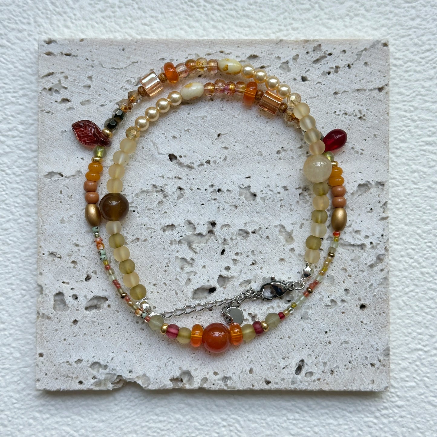 Flat lay of Golden Nectar Necklace on textured card – warm amber and gold palette with petite leaf accent