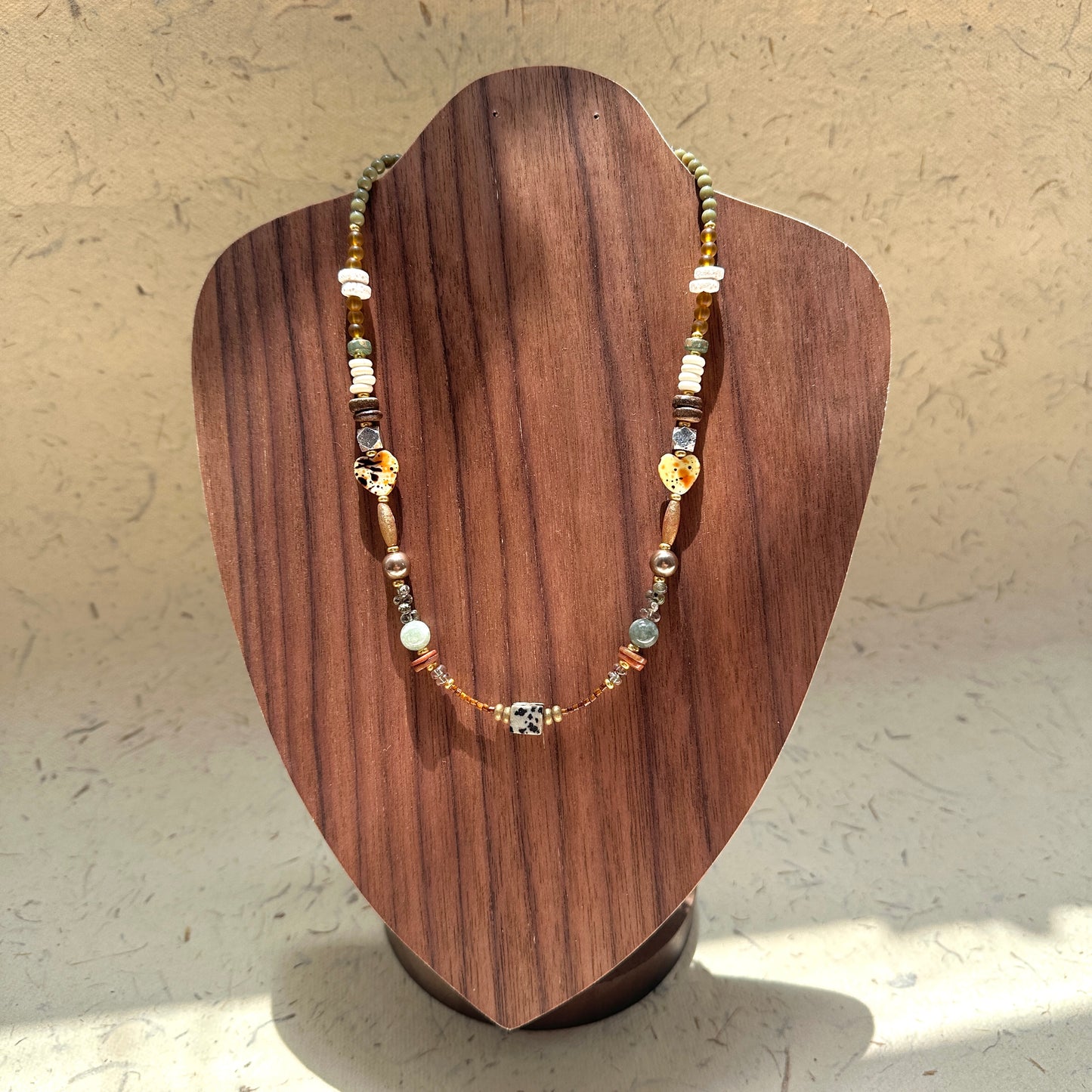 Sage & Saffron Necklace on wood display bust — sage-green and amber beads with speckled heart accents and a dotted cube focal