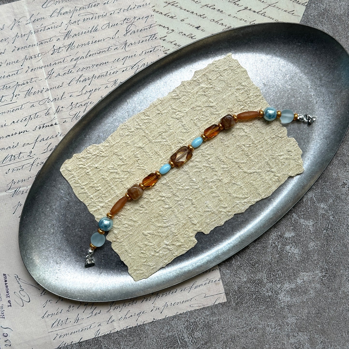 Aqua & Amber Drift Bracelet — flat lay on textured stone paper; sea-glass aqua and warm amber beads with gold accents and a nickel-free magnetic clasp 3