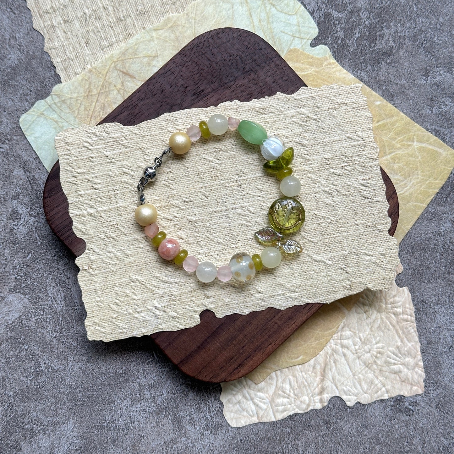 Citron Bloom Bracelet — flat lay on layered yellow papers; lemon-yellow and olive-green beads with citrus-style focal and leaf accents 3