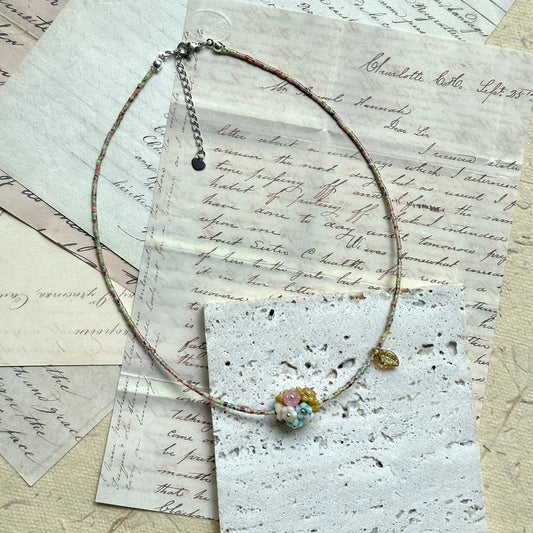 Blossom Garden Necklace — flat lay on vintage papers; multicolor seed beads, floral lampwork focal, golden leaf charm