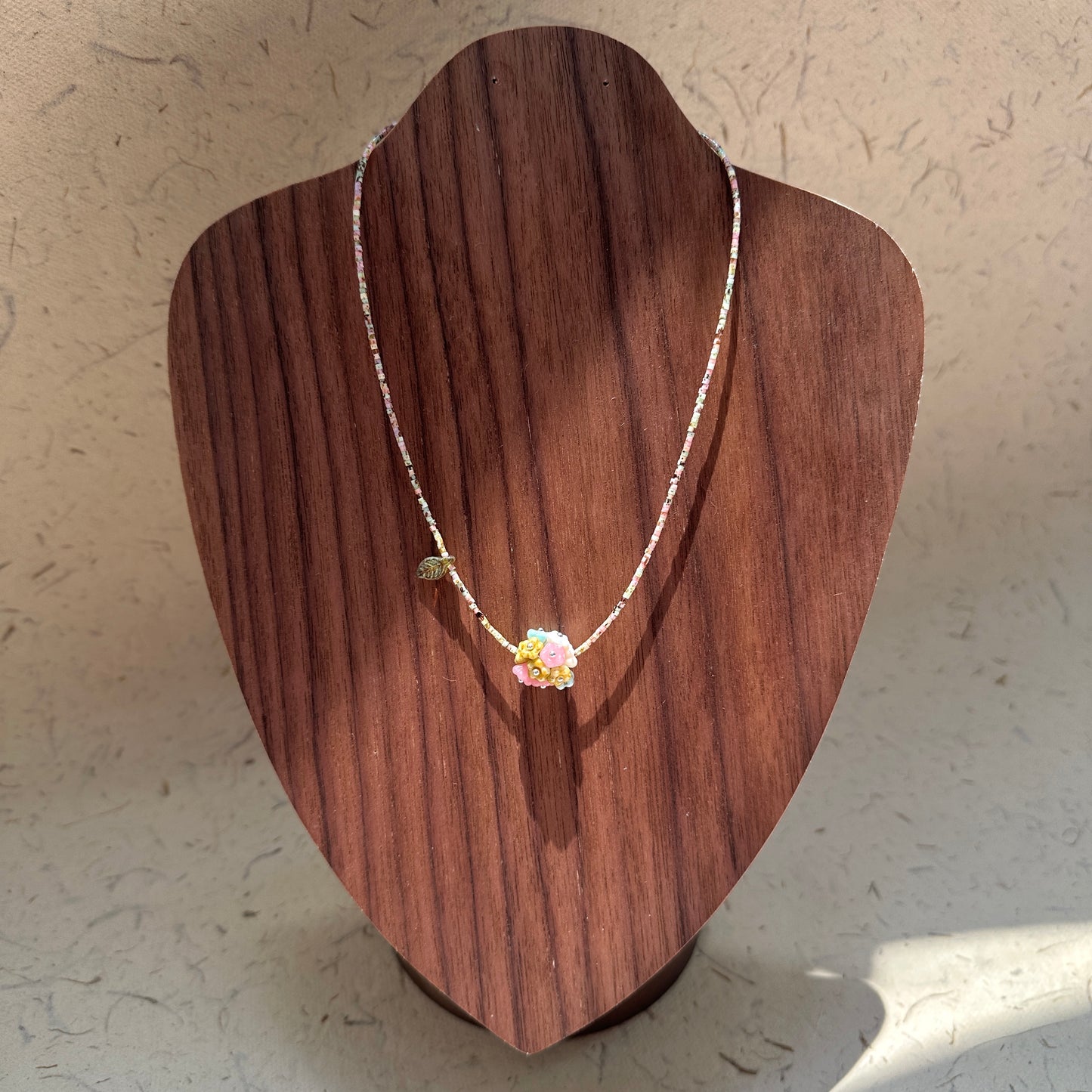 Blossom Garden Necklace on wood display bust — floral lampwork focal, golden leaf charm