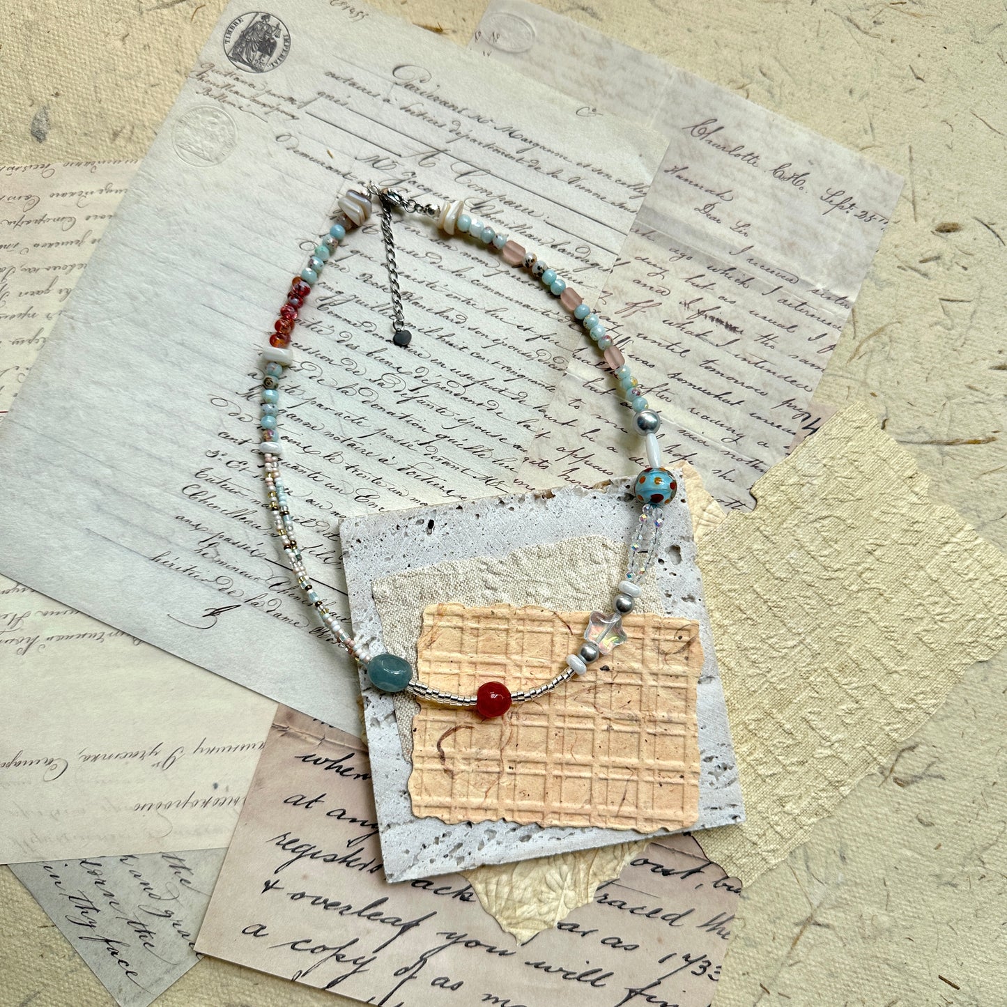 Candy Sky Necklace — flat lay on vintage papers; pastel glass beads with red and blue accents, star charm, polka-dot lampwork bead