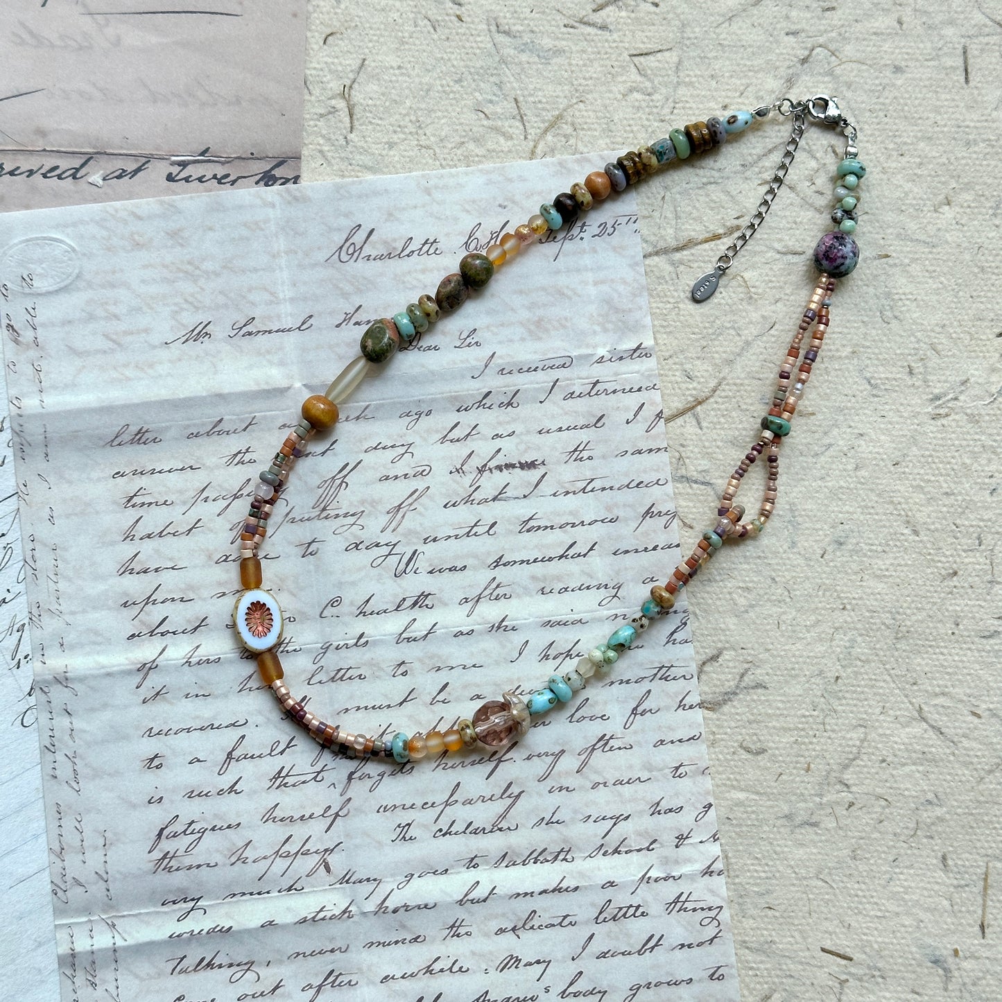 Sunlit Meadow Necklace — flat lay on vintage papers; warm amber and earthy-green glass beads with a sunflower-inspired focal