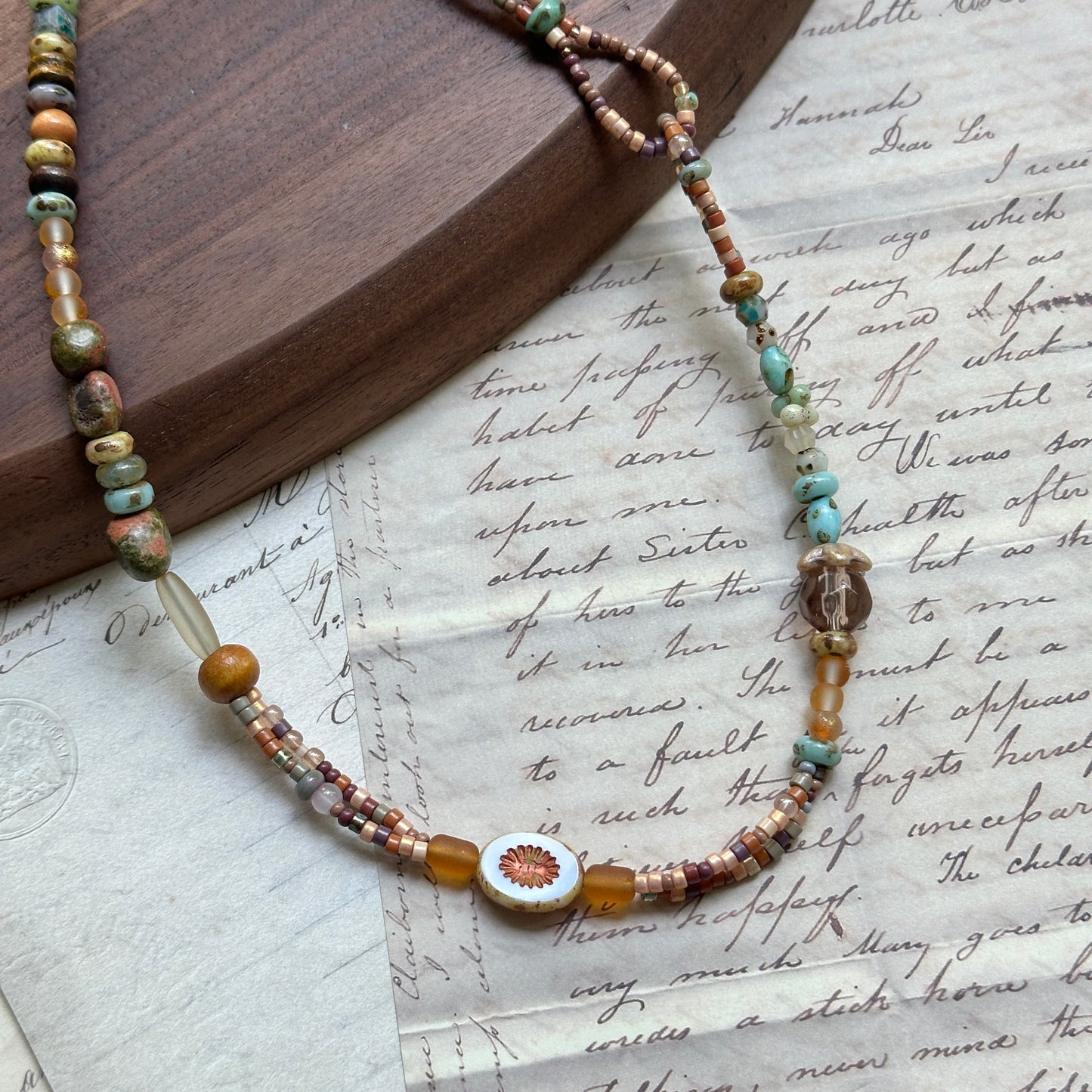 Sunlit Meadow Necklace — circle layout on textured paper; arrangement of amber and green glass beads with sunflower detail