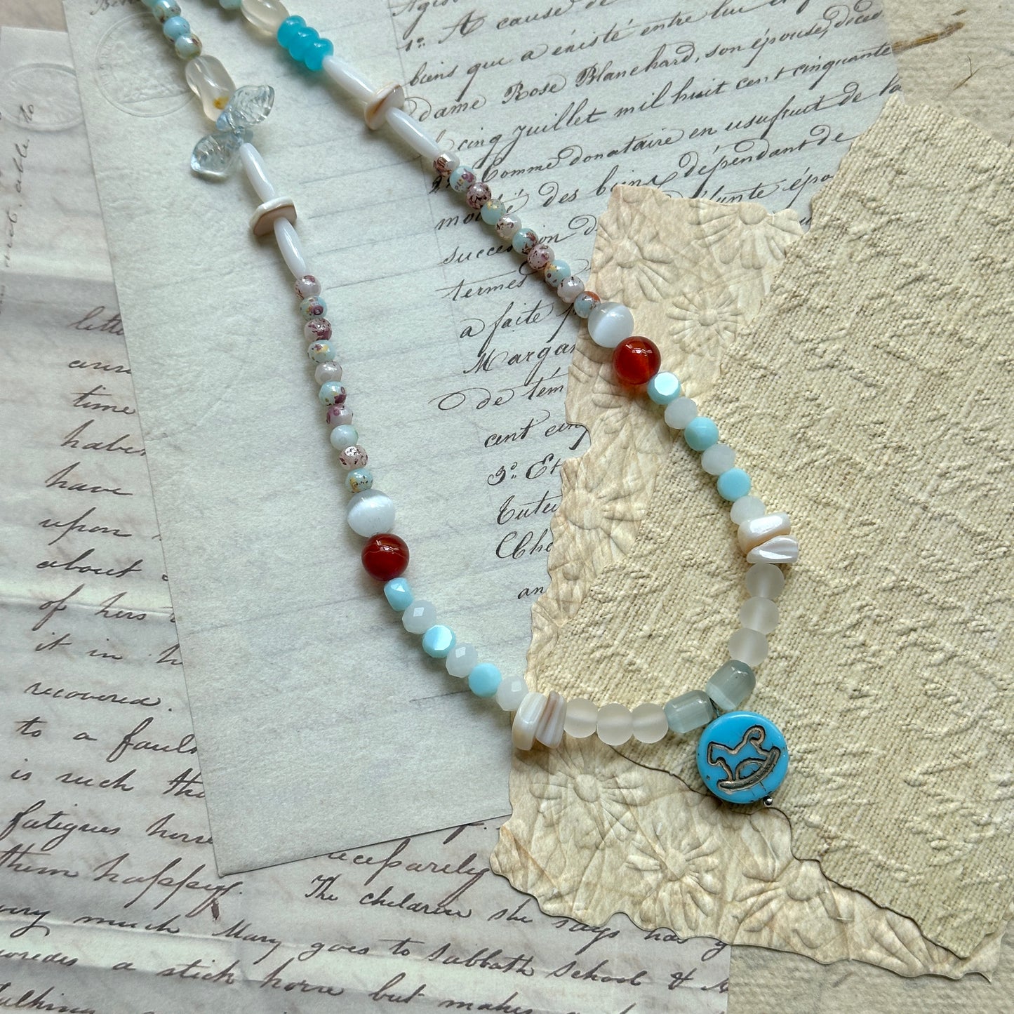 Dolphin Tide Necklace — close-up showing the dolphin medallion, seafoam-blue beads, pearl-white beads, and coral-red accents