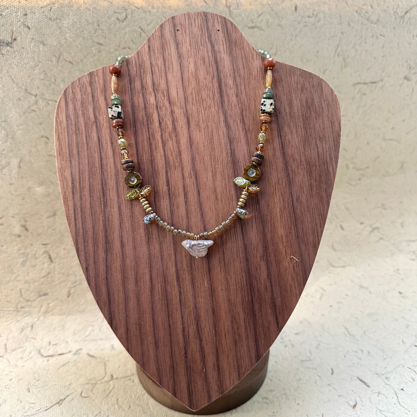 Amber Leaf Trail Necklace on wood display bust — amber and olive beads with tiny glass leaves and a clear chip pendant