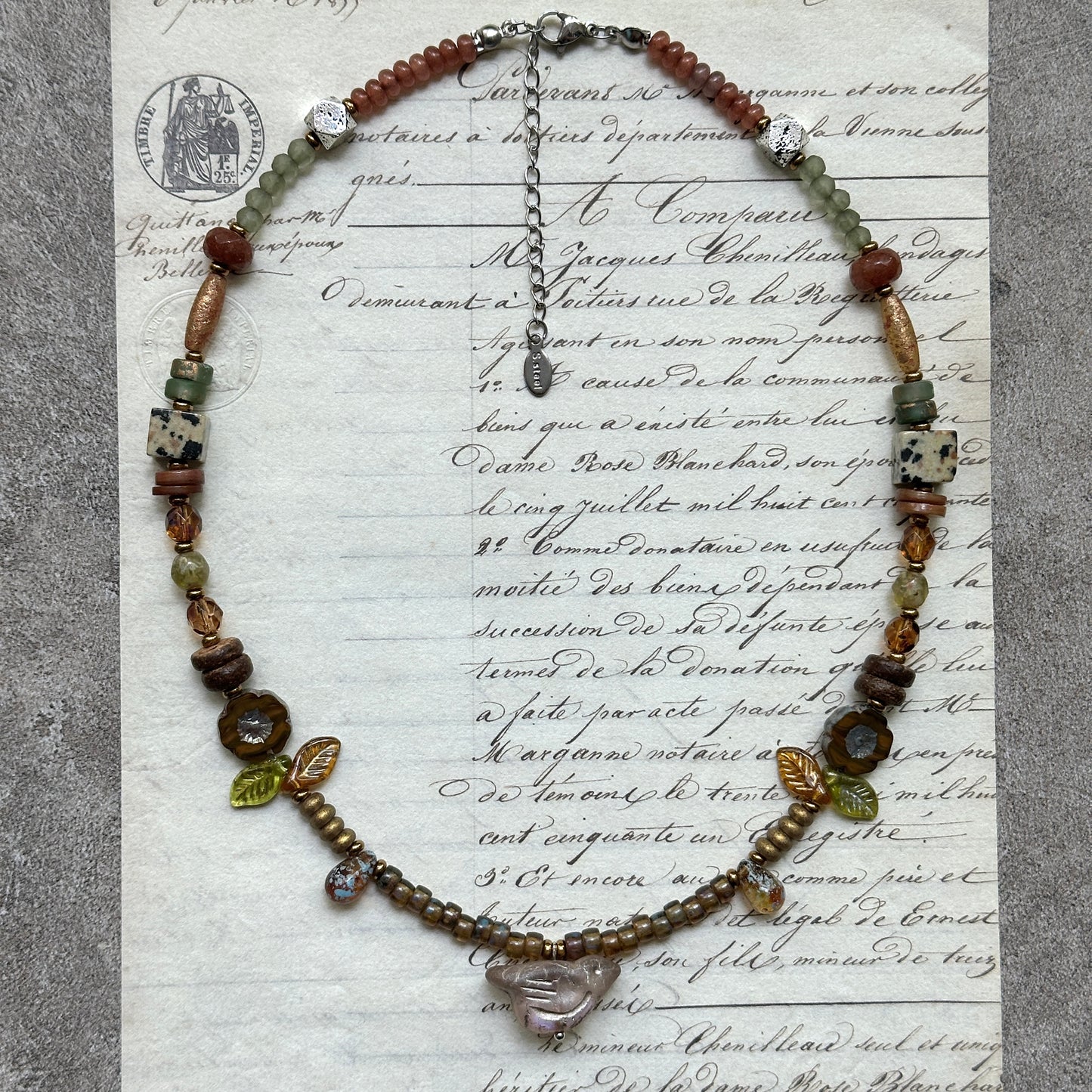 Amber Leaf Trail Necklace — flat lay on textured papers; amber/olive palette with leaf accents and clear pendant