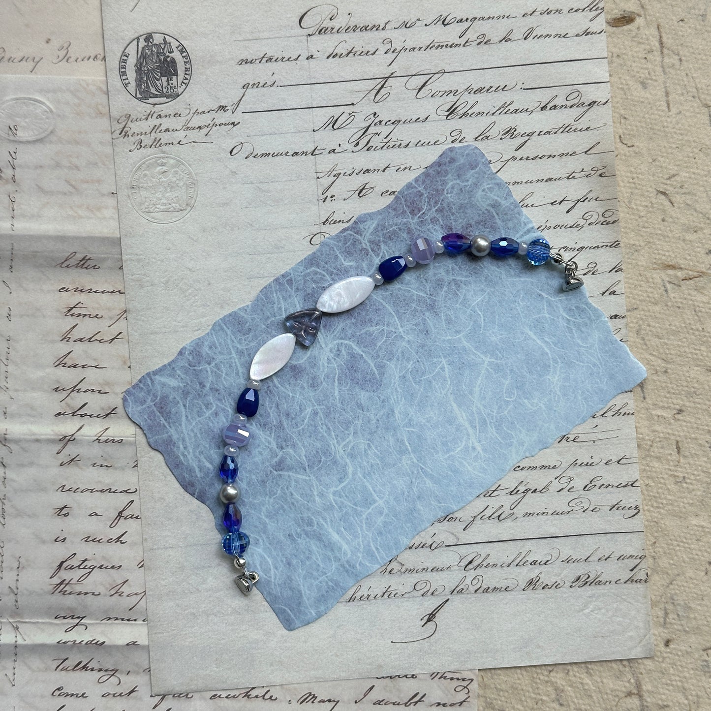 Elegant Midnight Pearl Bracelet featuring sapphire blue crystals, lilac accents, and iridescent pearl-white beads, styled flat on vintage letter paper background.