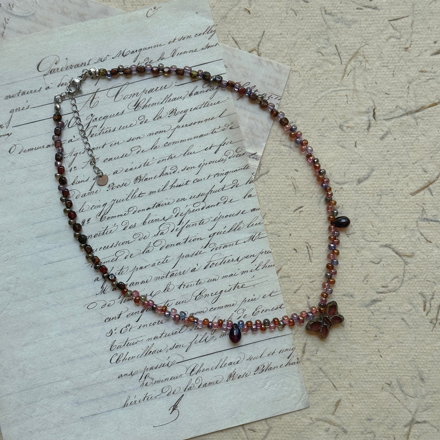 Twilight Bloom Necklace by Glazenya – handcrafted beaded necklace in wine-red, plum, and amber tones with a floral charm, displayed on vintage letter background.