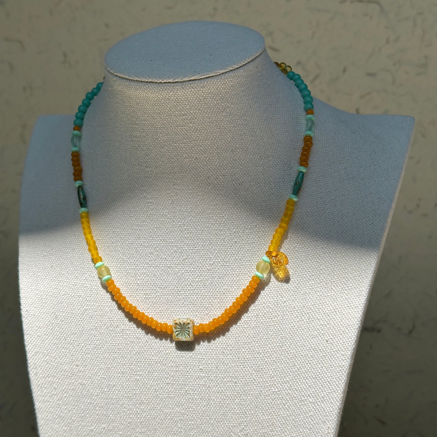 Citrus Lagoon Necklace worn on bust, showcasing fresh summer palette of yellow and green beads with floral ceramic and amber leaf details