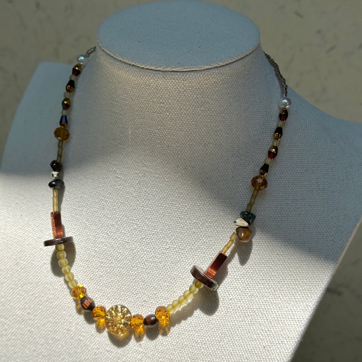 Marigold Ember Necklace worn on bust, highlighting golden sunburst bead with warm amber-yellow and earthy green-brown tones