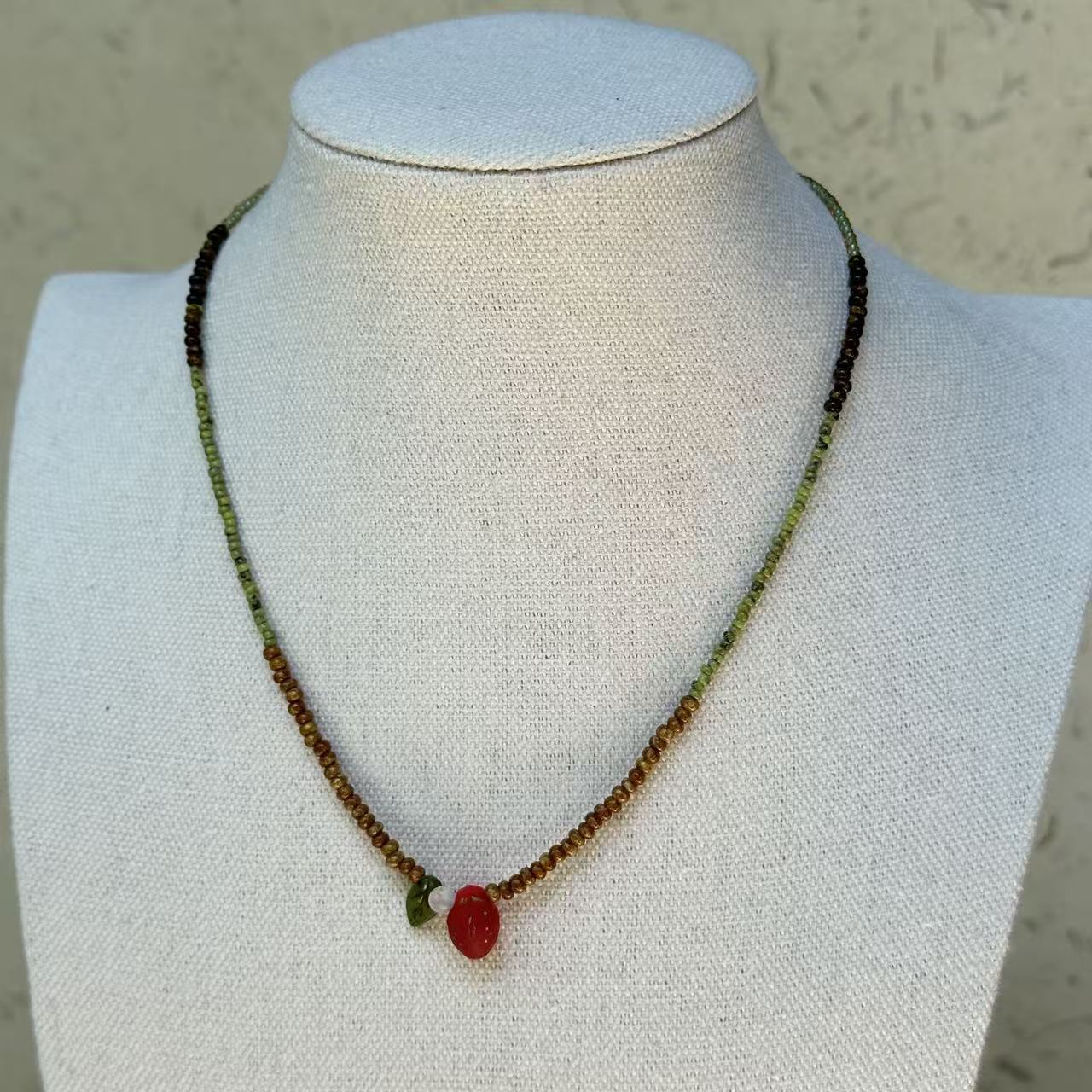 Wild Strawberry Necklace worn on bust, showcasing playful red glass strawberry pendant with delicate leaf detail and natural bead palette