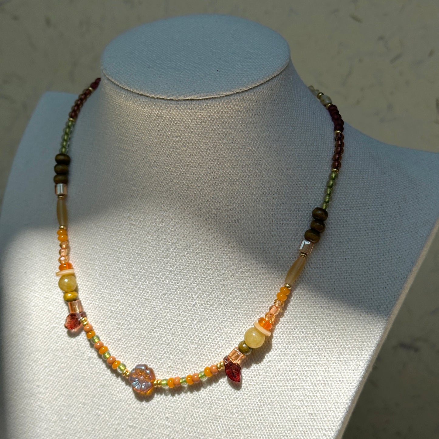 Olive Grove Blossom Necklace worn on bust, showcasing luminous glass flower pendant with earthy amber and olive-green beads