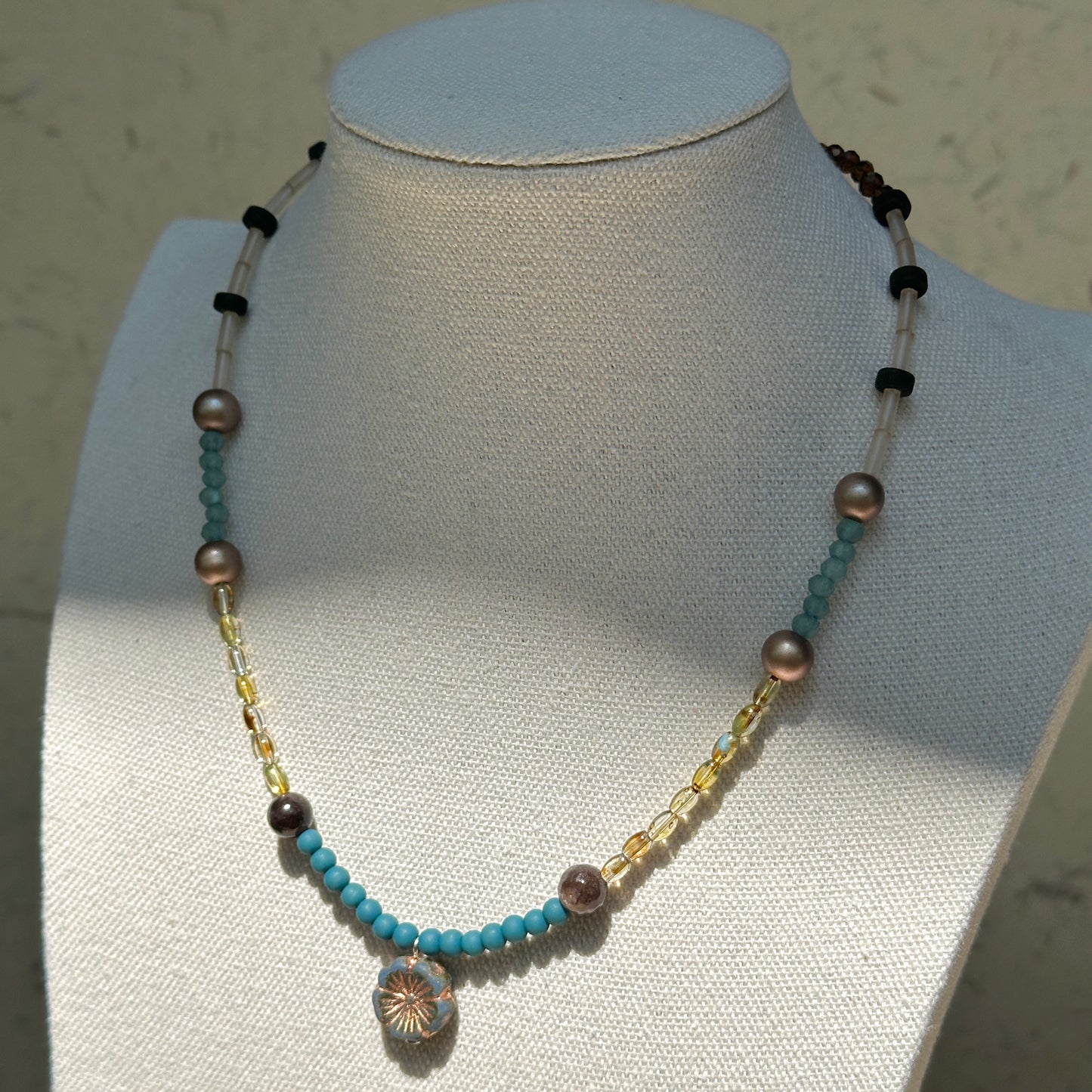 Lagoon Sunburst Necklace worn on bust, highlighting aqua-blue seed beads with gold details and sunburst medallion centerpiece