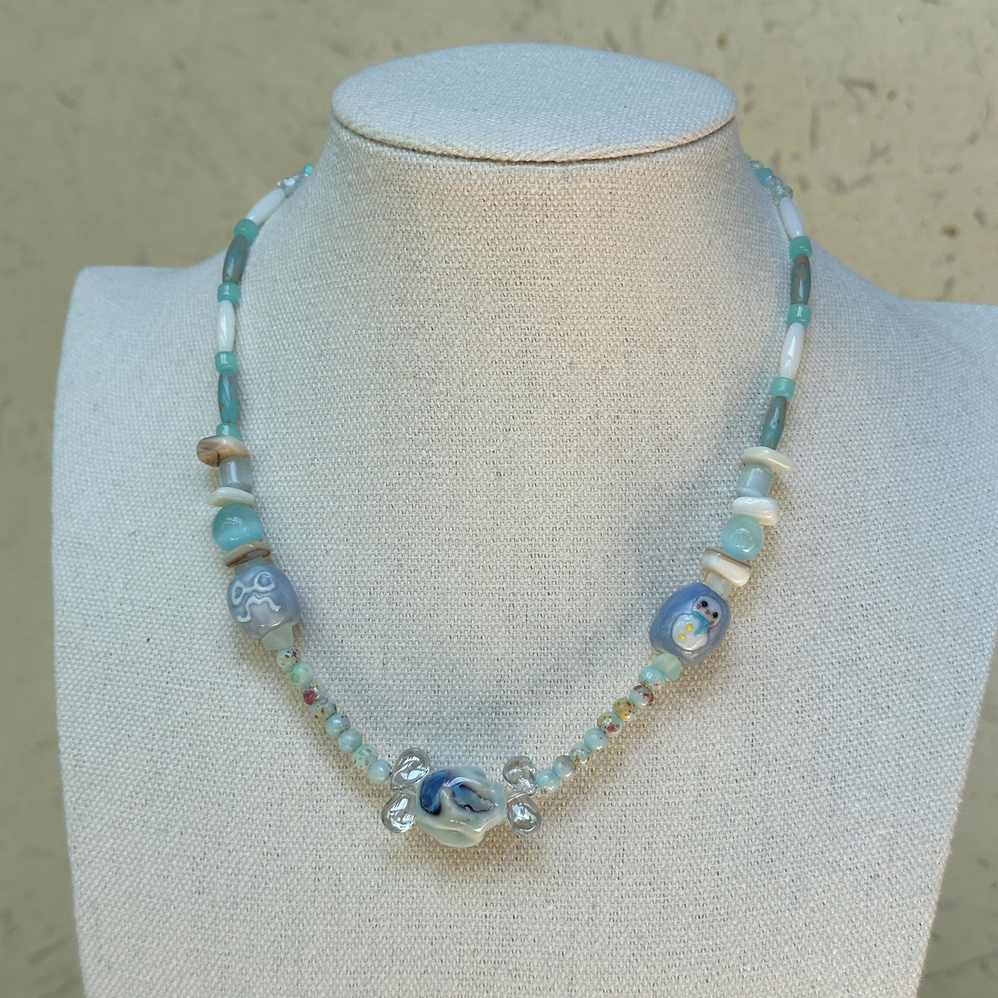 Ocean Whisper Necklace worn on bust, featuring soothing aqua and white palette with glass penguin and jellyfish charms for a coastal style