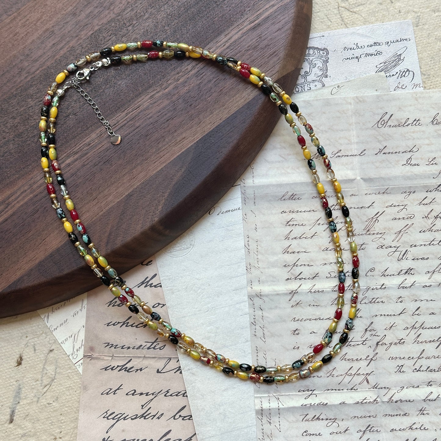 Tribal Glow Necklace close-up on rustic paper, featuring vibrant glass beads in red, yellow, green, and black with double-layer design