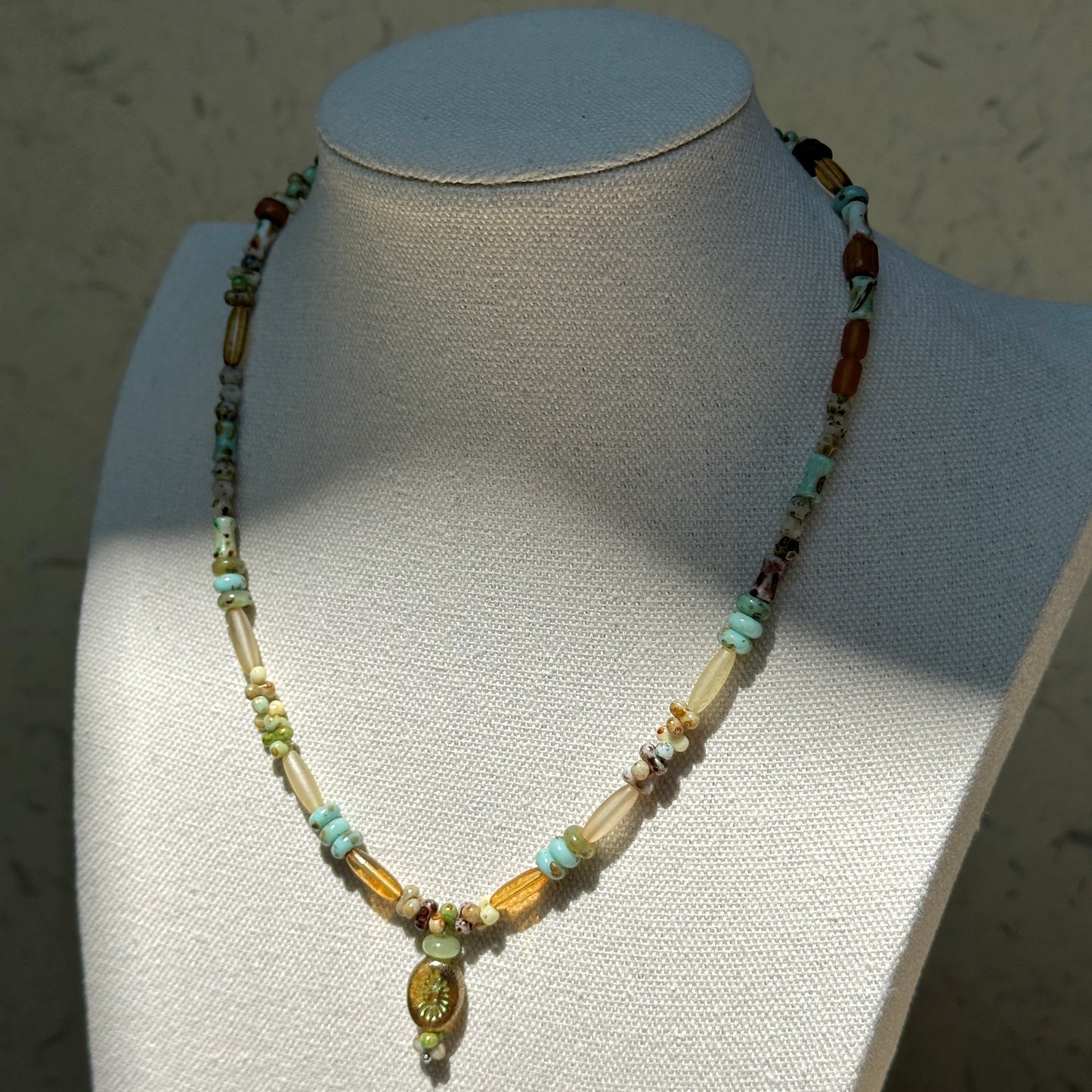 Verdant Amulet Necklace worn on bust, featuring amulet-style focal pendant with earthy green and amber-gold beads
