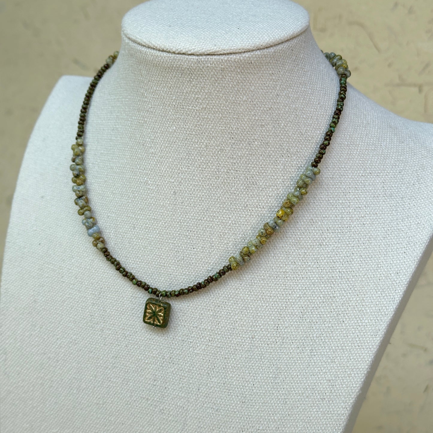 Gilded Bloom Necklace worn on bust, showing elegant golden and dark bead strand with engraved square floral charm