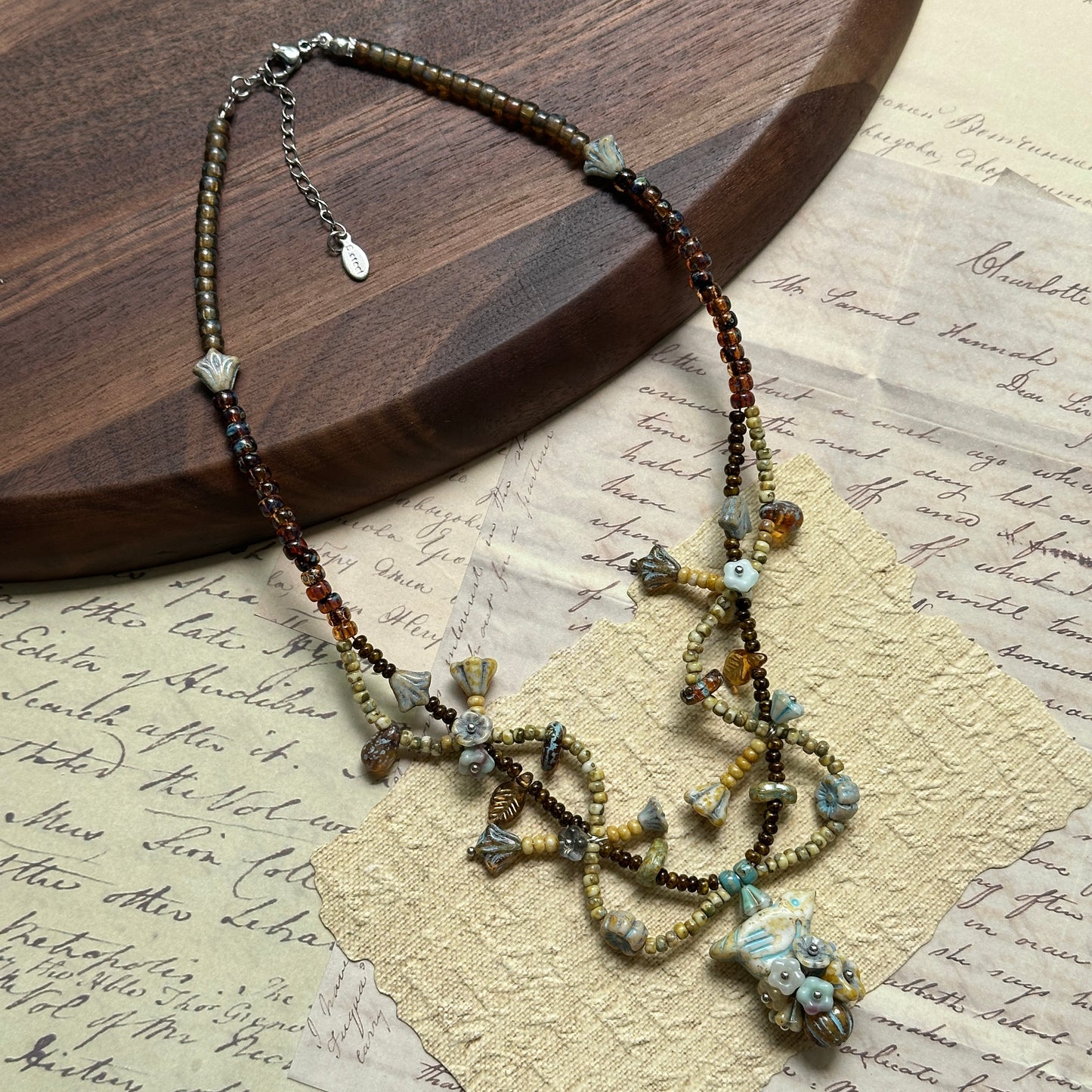 Artisan beaded necklace with amber glass, Czech beads, and leaf-inspired charms, arranged in circular form on white surface.