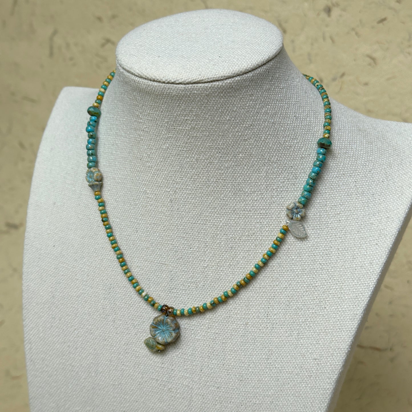 Lake Blossom Necklace worn on white bust display, highlighting turquoise beads, golden-yellow accents, and delicate floral pendant with leaf details.