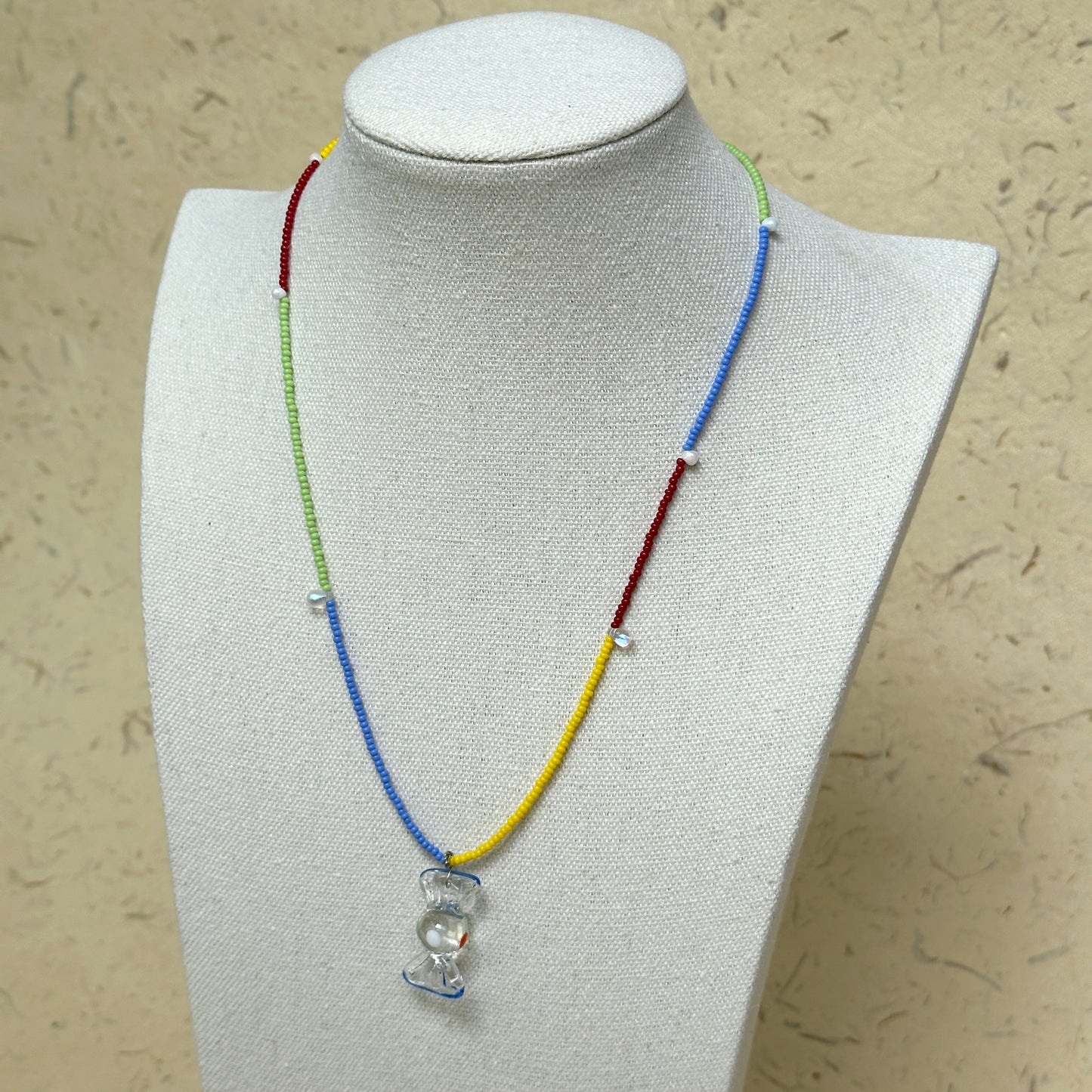 Joyful Hour Necklace worn on white bust display, highlighting rainbow seed beads and hourglass-style pendant centerpiece.