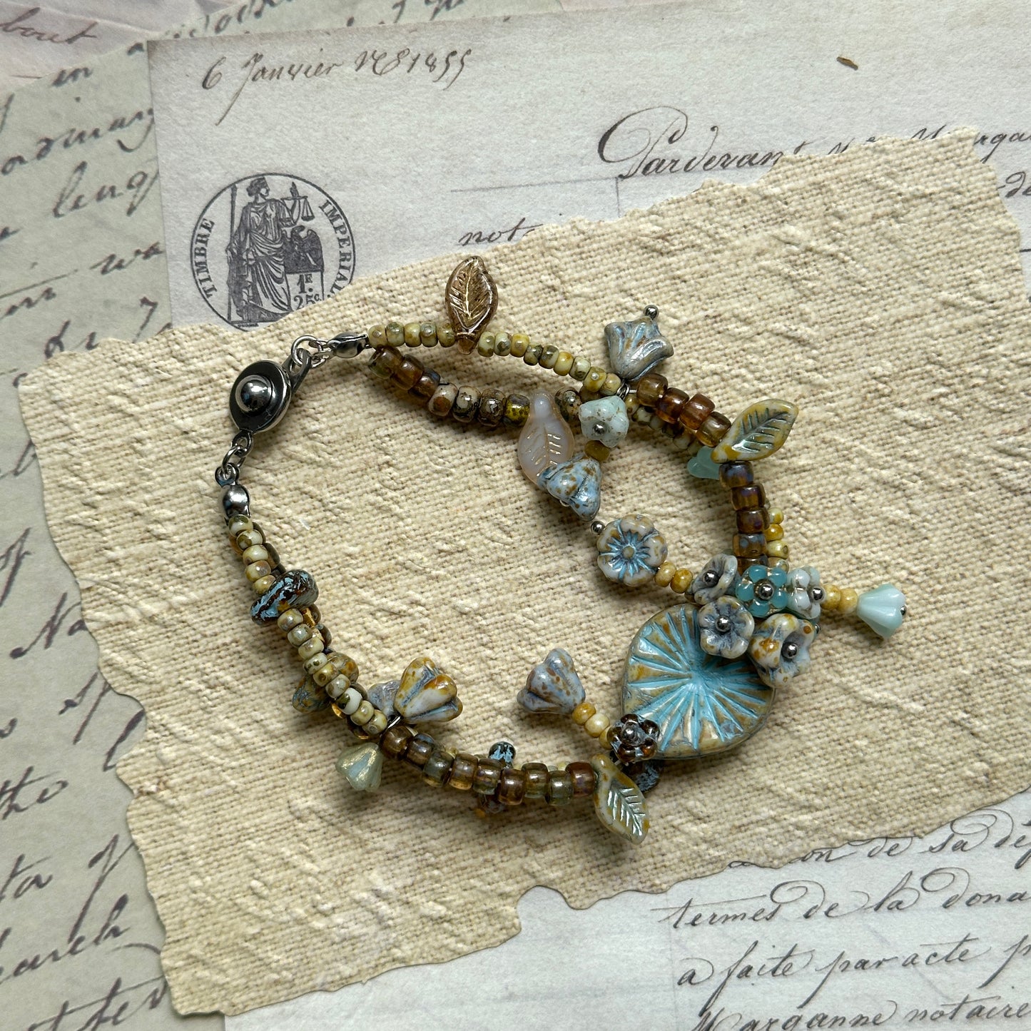 Blue Garden Bracelet featuring delicate blue beads and vintage-inspired floral and leaf charms, handcrafted in earthy beige and golden hues.