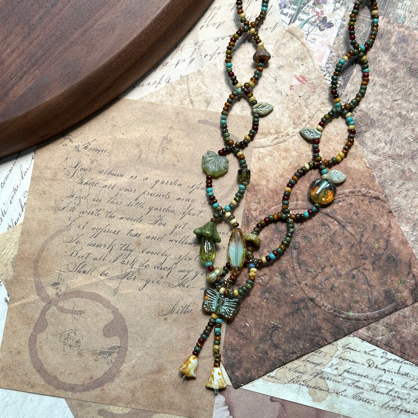Detail of butterfly tassel and pressed-glass leaf charms on the Olive Grove Lariat Necklace; airy, botanical feel.