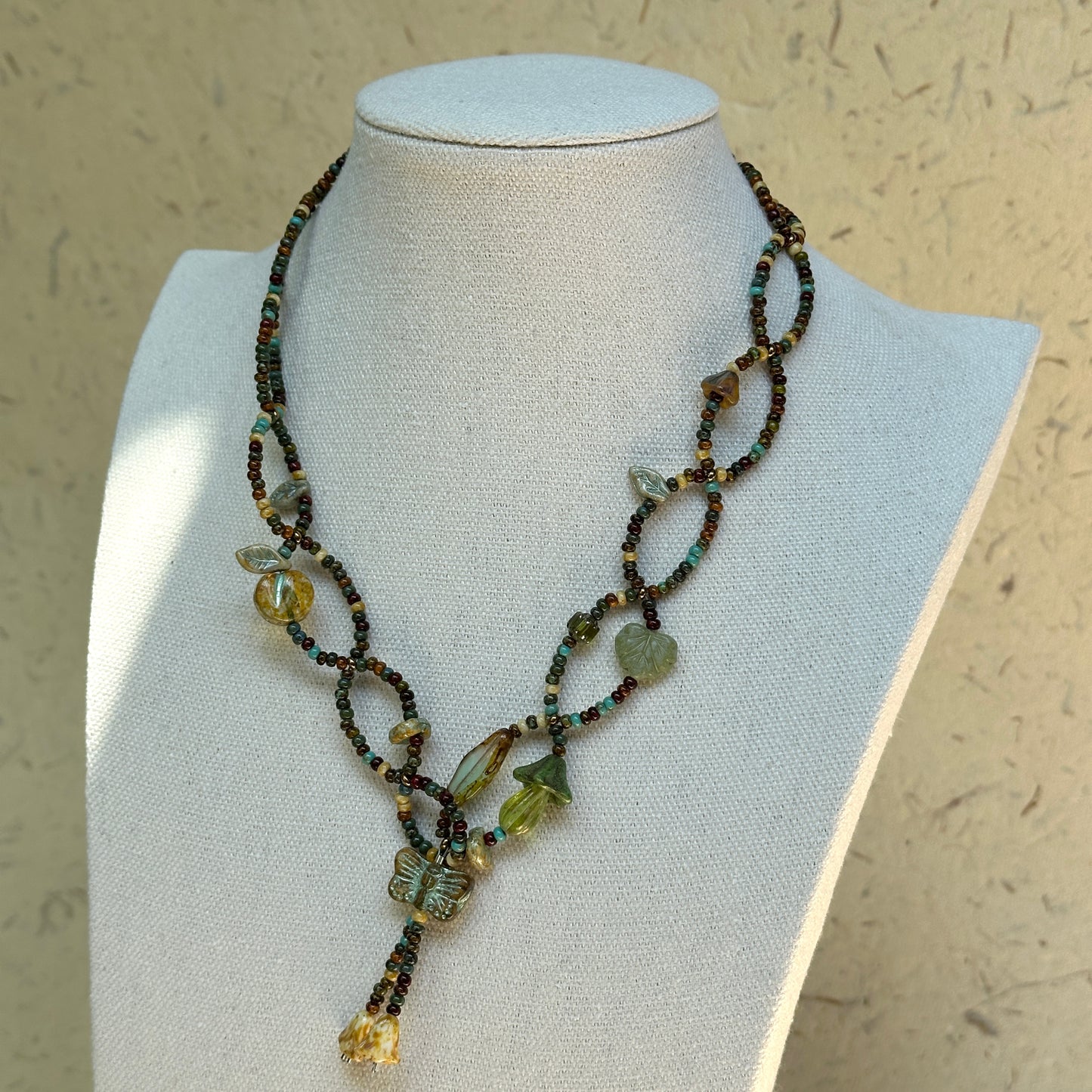 Olive Grove Lariat Necklace on a mannequin, draped lariat silhouette with adjustable drop; olive, moss and warm amber tones.