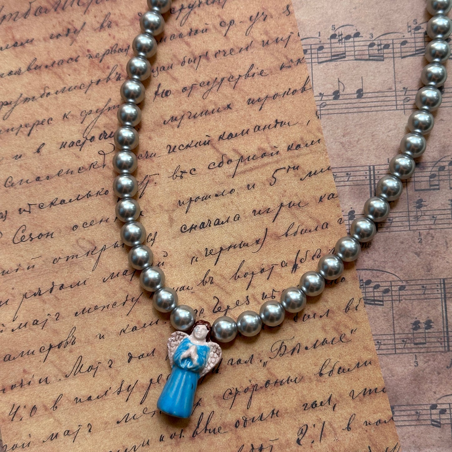 Close detail of Angel’s Grace Necklace—luminous faux-pearl strand with sky-blue glass angel charm pendant.