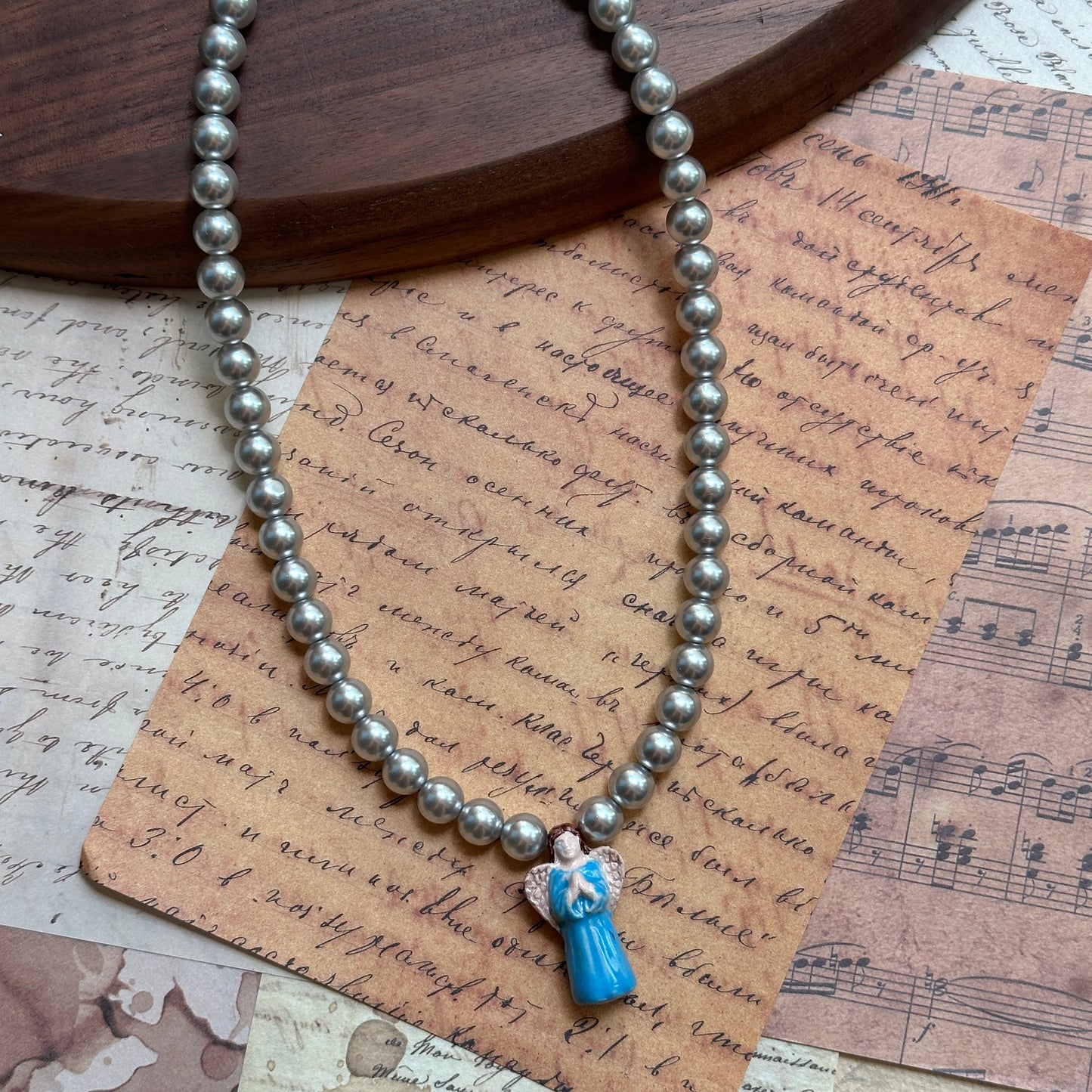 Angel’s Grace Necklace coiled flat lay showing full faux-pearl strand and petite sky-blue angel charm.
