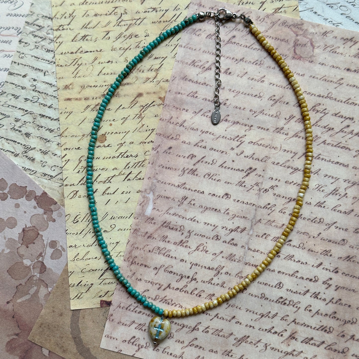 Faithlight Necklace coiled flat lay showing full two-tone strand with a delicate glass cross pendant at center.