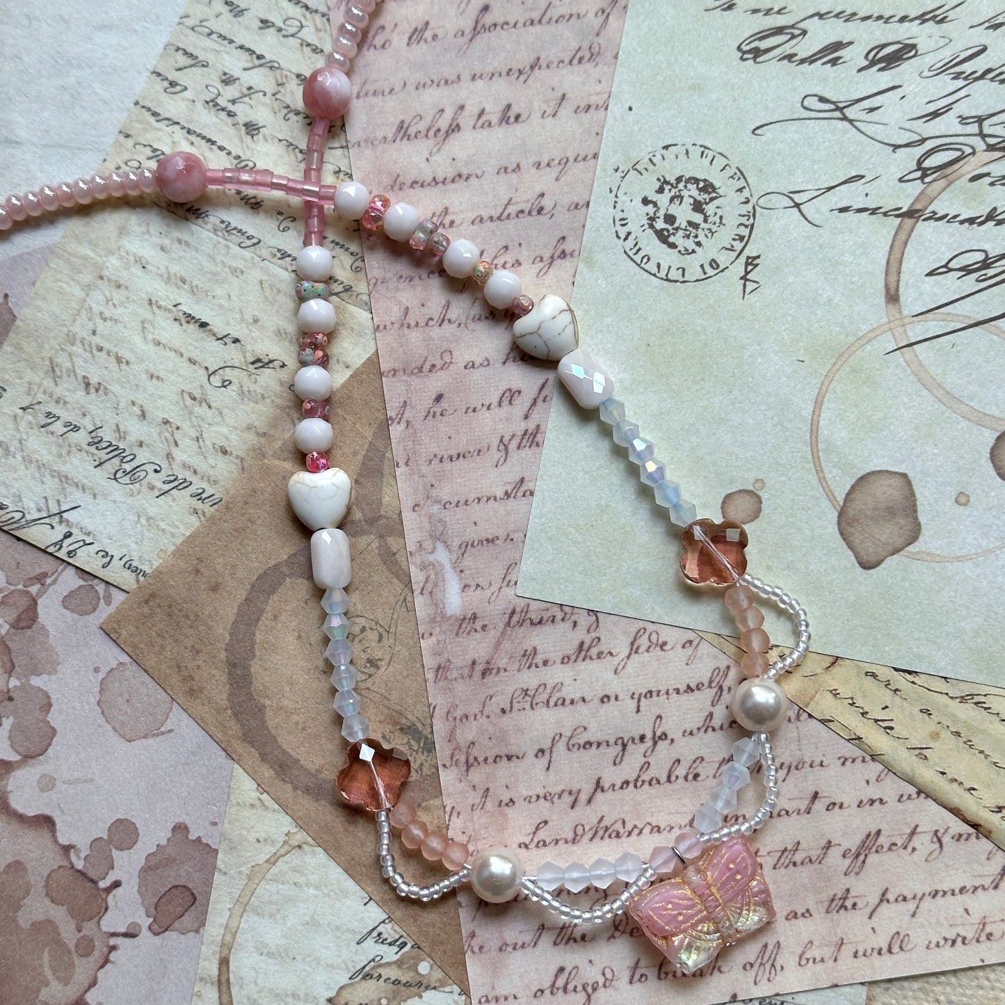 Blush Wing Necklace coiled flat lay showing full strand with blush butterfly pendant, bead drapes, champagne crystal flowers and pearls.