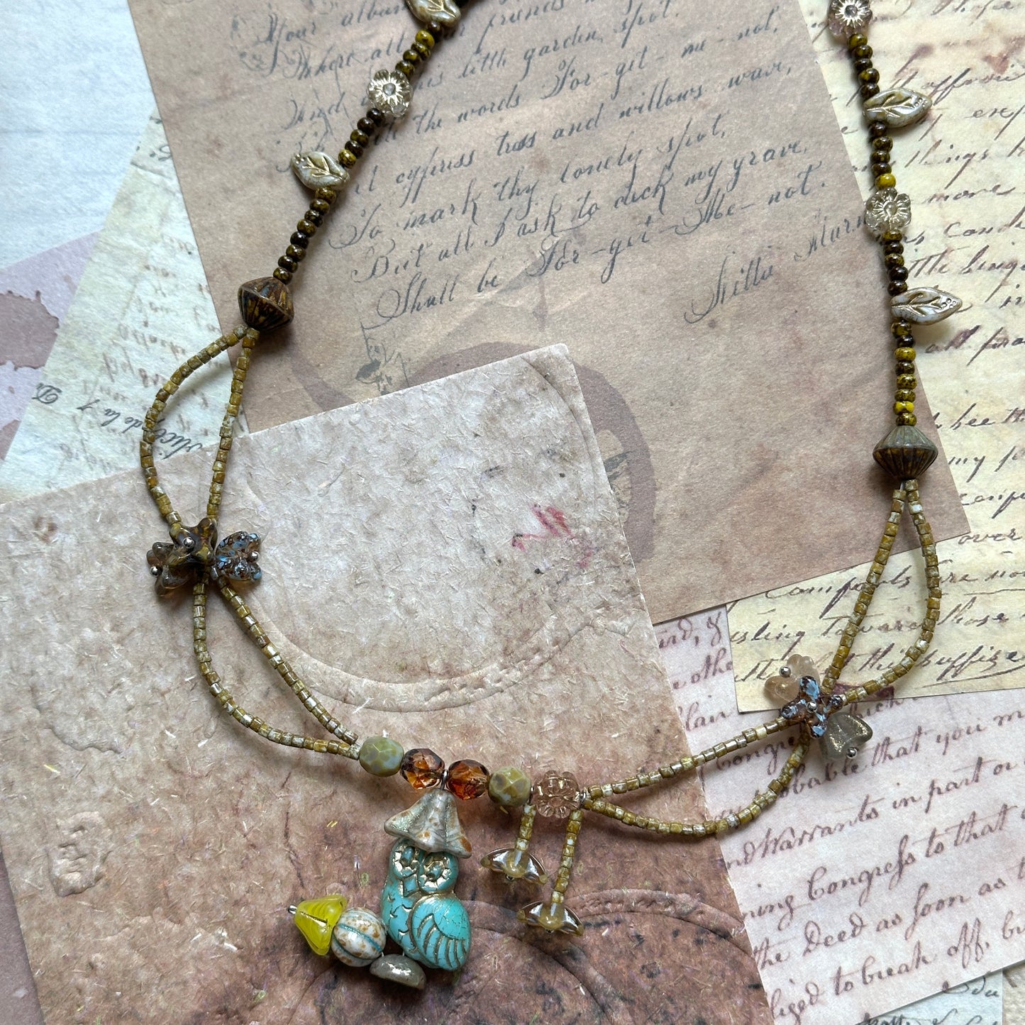 Woodland Spirit Necklace coiled flat lay showing full strand, turquoise leaf focal and warm woodland palette with subtle gold-tone accents.