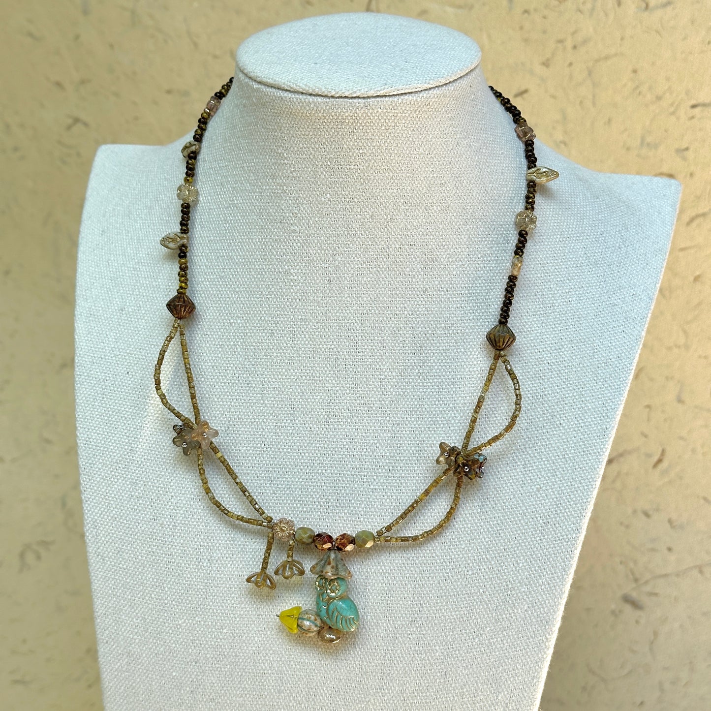 Woodland Spirit Necklace on mannequin—turquoise glass leaf pendant with flower charms and earthy amber/brown beads; lightweight and easy to wear.