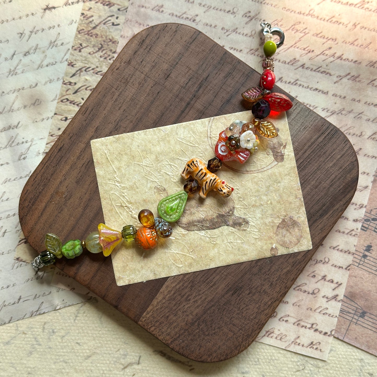 Tiger Orchard Bracelet artisan jewelry with tiger bead, amber, red, and green glass charms, styled on a rustic wooden board
