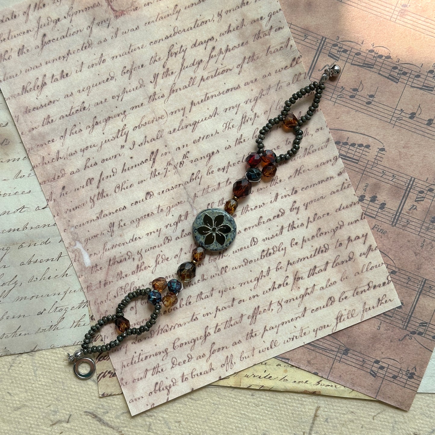 Close-up of Antique Flower Window Bracelet on textured fabric, metallic seed-bead ovals and bronze chain highlighting the vintage window motif