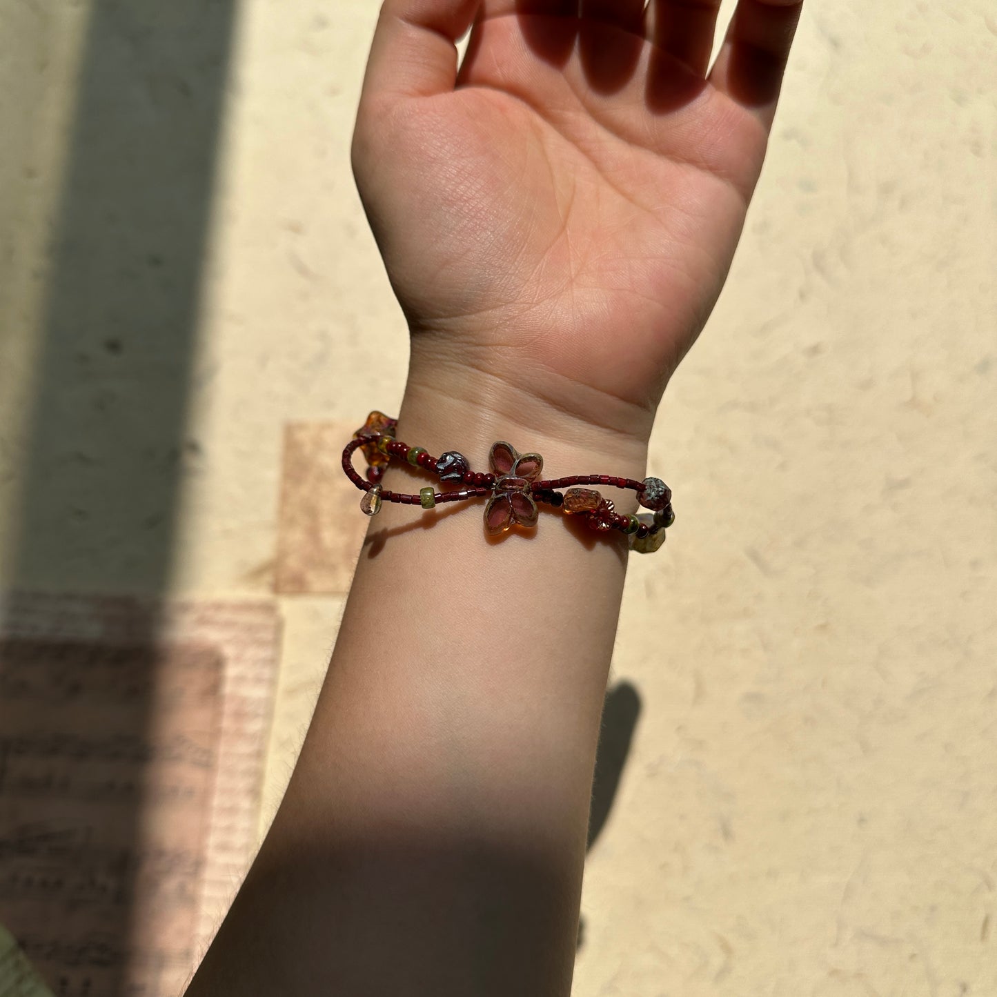 Close view on paper background, crimson butterfly bead with bronze chain and warm amber glass accents, moody midnight palette