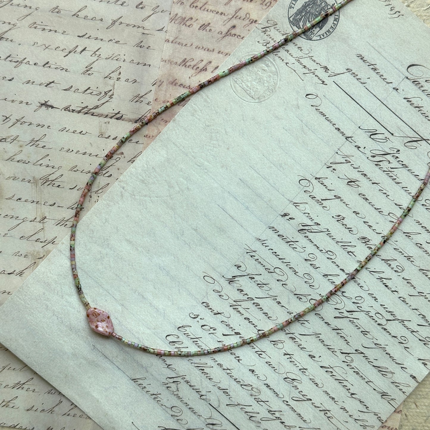 Close-up of pastel seed-bead strand with pink floral focal, lightweight minimalist design inspired by morning dew