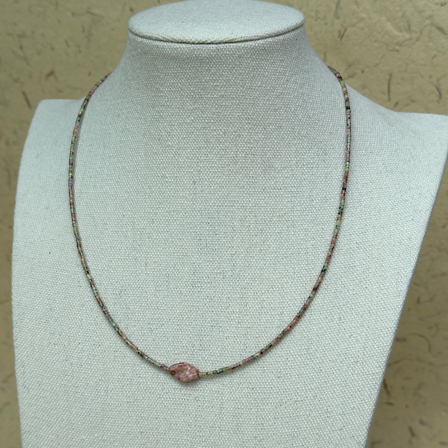 Necklace displayed on mannequin bust, soft green and pink seed beads with petite floral centerpiece, airy everyday layering piece