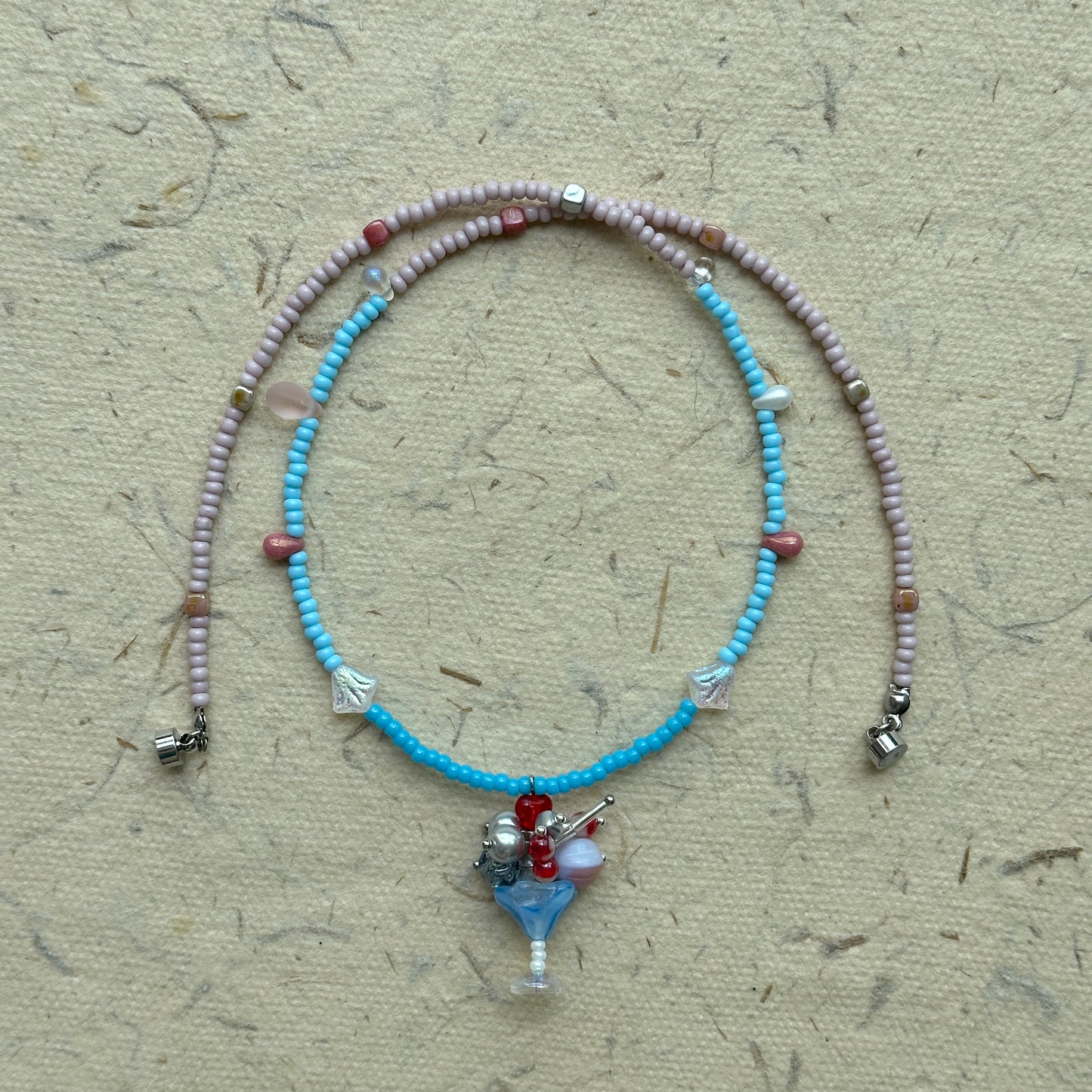 Necklace arranged in a circle, pastel pink and blue strand with floral charm pendant at the center
