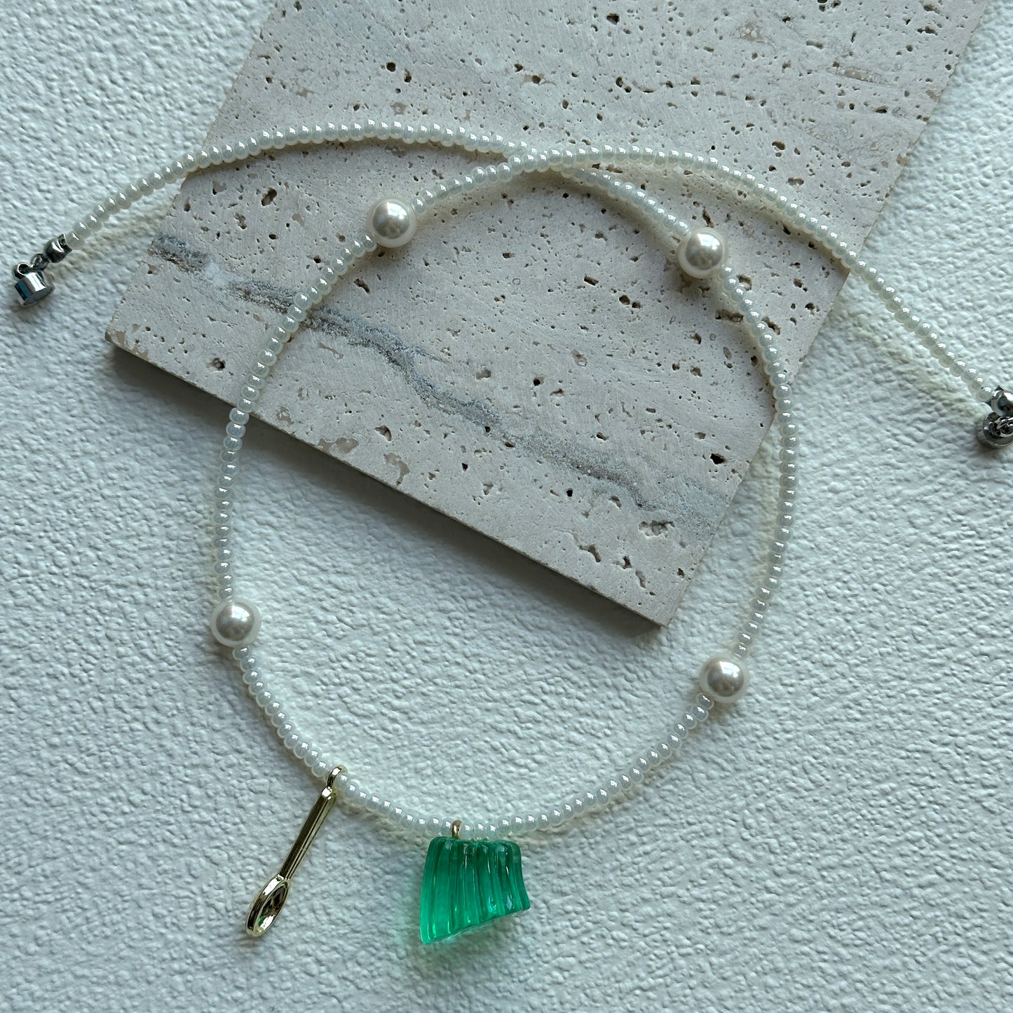 Gold-tone charm detail beside green pendant on necklace
