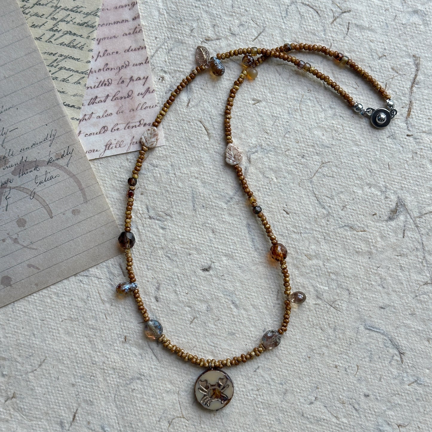 Close-up of crab motif round pendant with earthy brown beads