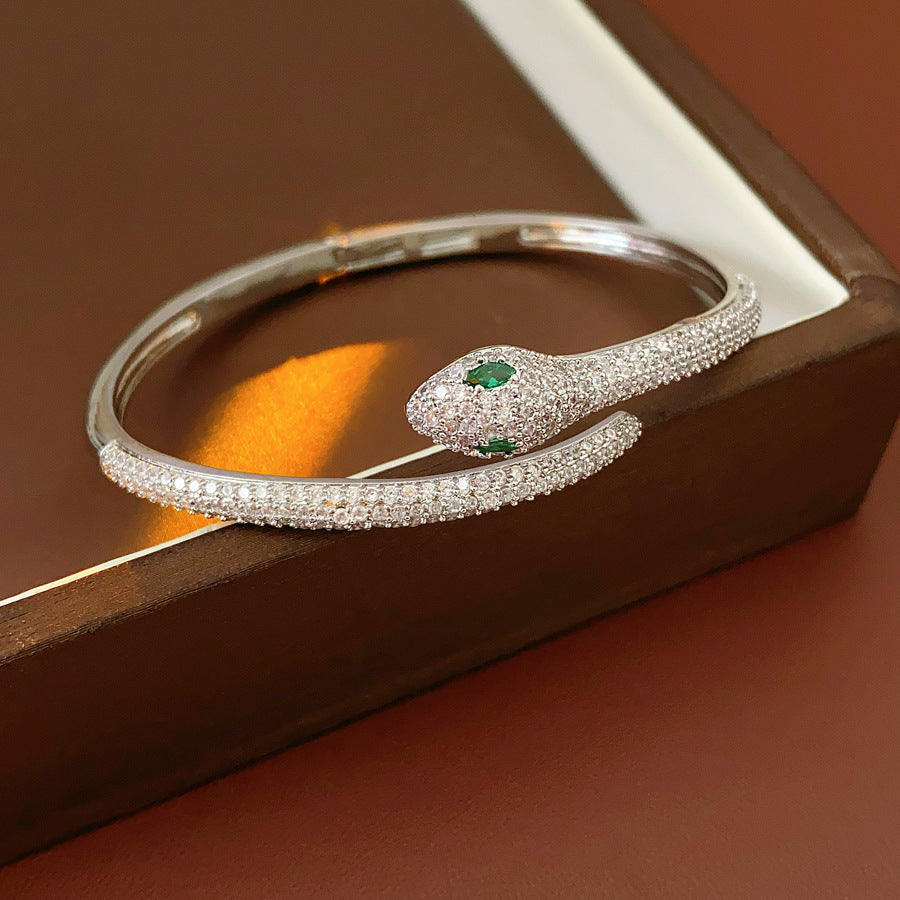 Gold and silver snake-shaped zircon bangles with emerald eyes — Serpent Luxe Bangle by Glazenya.