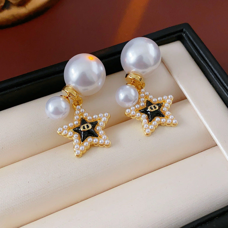 Double-pearl stud earrings with gold-tone butterfly and star charms displayed in a jewelry tray — Double Pearl Charm Studs.