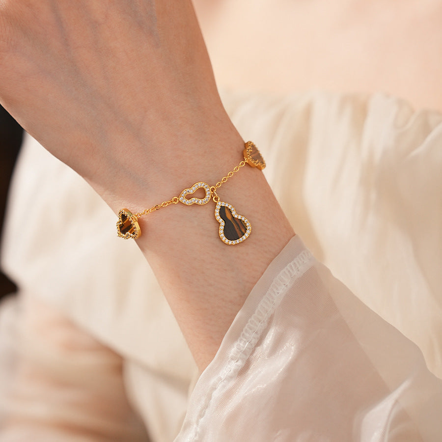 Fortune Gourd Tiger Eye Bracelet with golden gourd motifs, cubic zirconia accents, and natural tiger eye stones, displayed on red wood background