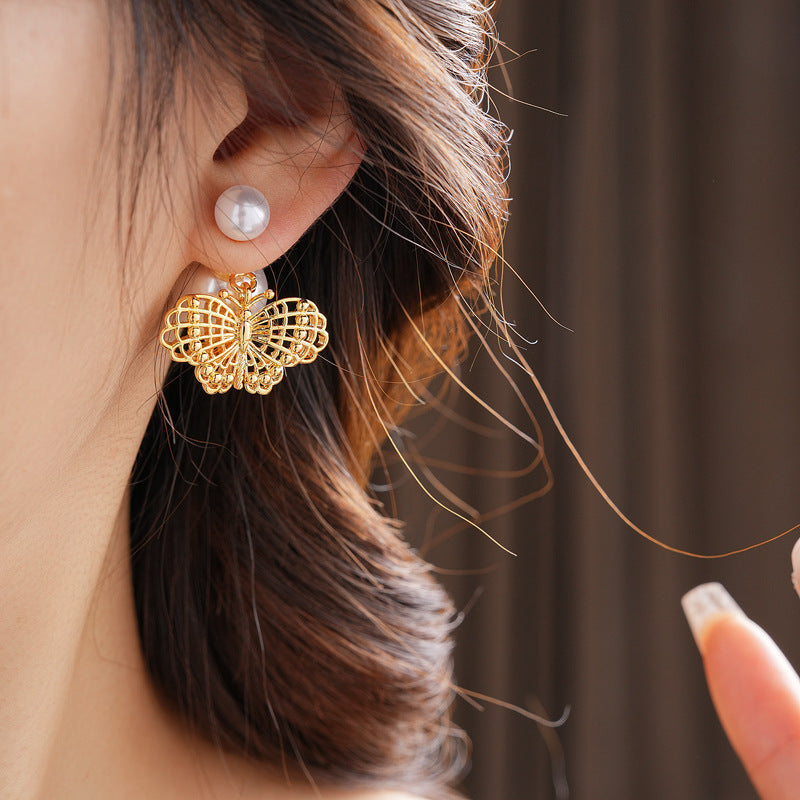 Double-pearl stud earrings with gold-tone butterfly and star charms displayed in a jewelry tray — Double Pearl Charm Studs.