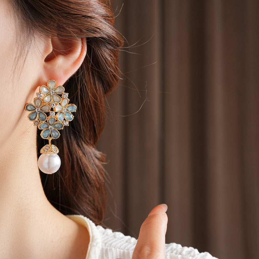 Gold floral cluster earrings with ice-blue petals, crystal accents, and a single luminous faux-pearl drop — Ethereal Petal Pearl Earrings.