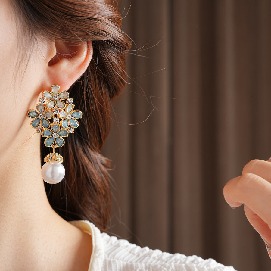 Gold floral cluster earrings with ice-blue petals, crystal accents, and a single luminous faux-pearl drop — Ethereal Petal Pearl Earrings.