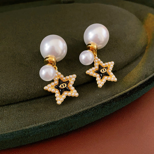 Double-pearl stud earrings with gold-tone butterfly and star charms displayed in a jewelry tray — Double Pearl Charm Studs.